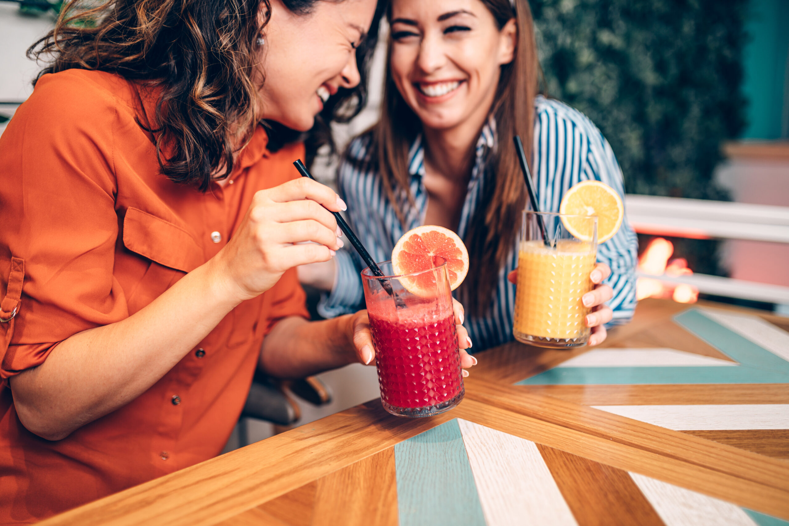Two women enjoying citrus-based non-alcoholic mocktails enhanced with naringenin and natural flavor modulators at a modern café.